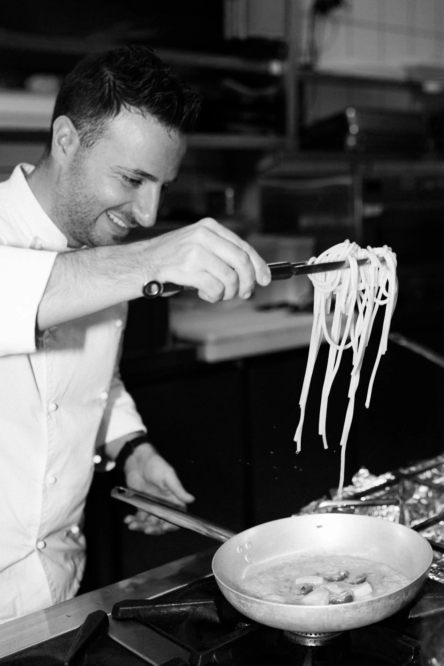 Fokussierte Schwarz-Weiß-Detailaufnahme im Buonissimo Neu-Ulm: Ein lächelnder Koch bereitet leidenschaftlich eine Pasta zu.